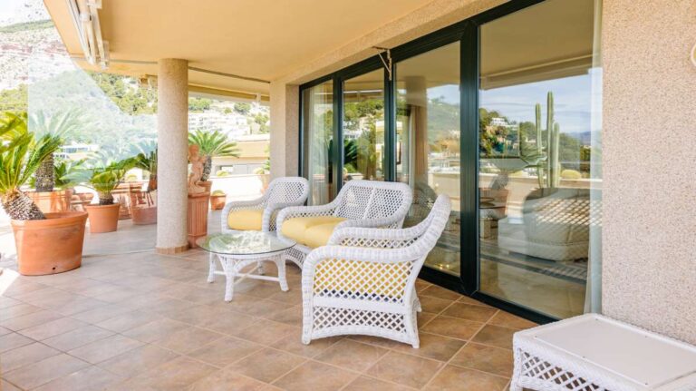 Covered terrace lounge at a luxury apartment in Sierra de Altea with outdoor chairs, potted plants, sliding doors and shaded seating area