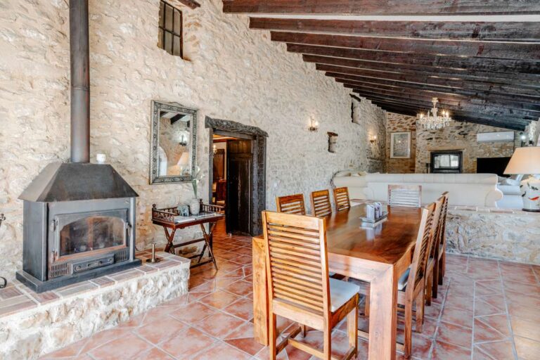 Dining area inside a historic luxury finca in Benissa with stone walls, wooden beams, fireplace and traditional terracotta flooring