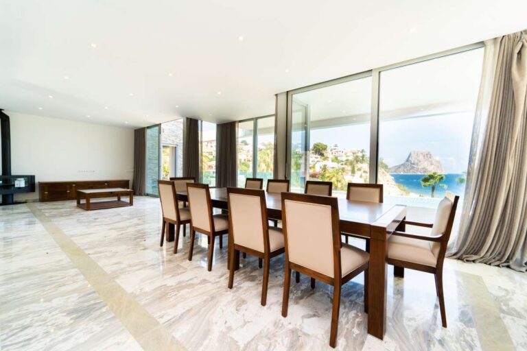 Dining area inside a luxury villa in Calpe with marble flooring, floor-to-ceiling windows and panoramic sea views towards the Peñón de Ifach