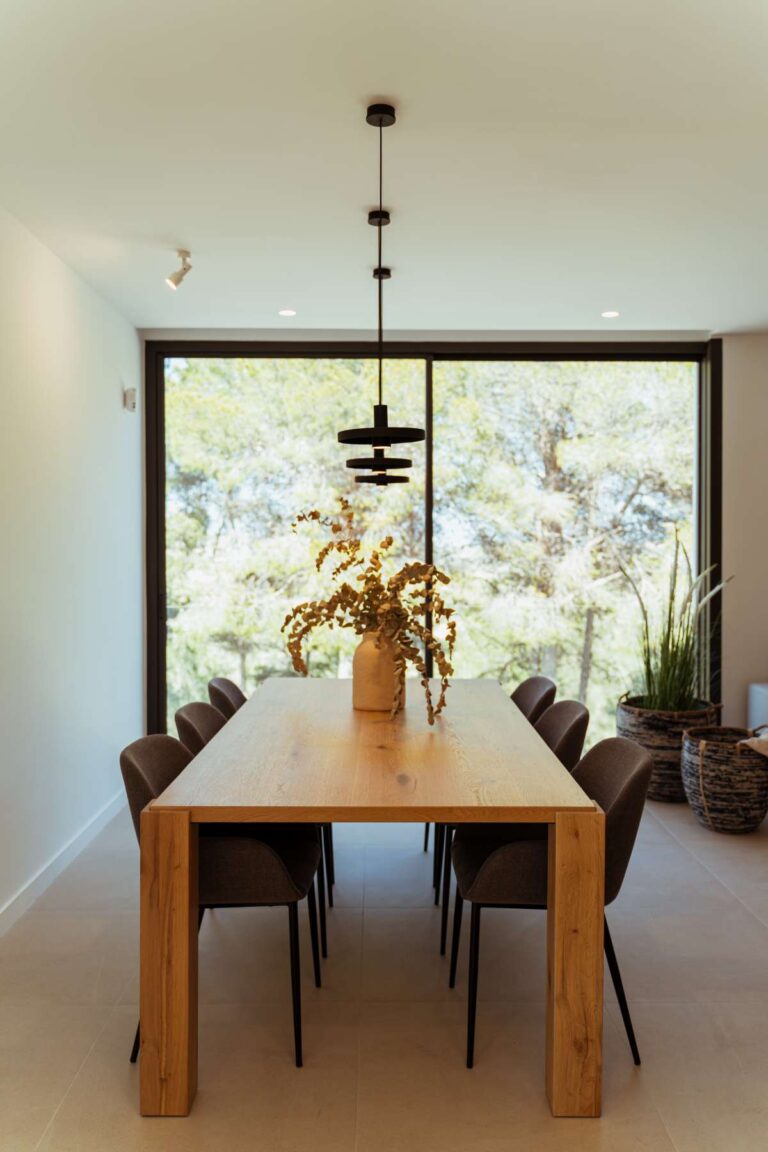 Dining area inside a new-build luxury villa in Moraira with wooden dining table, pendant lighting and large window overlooking greenery