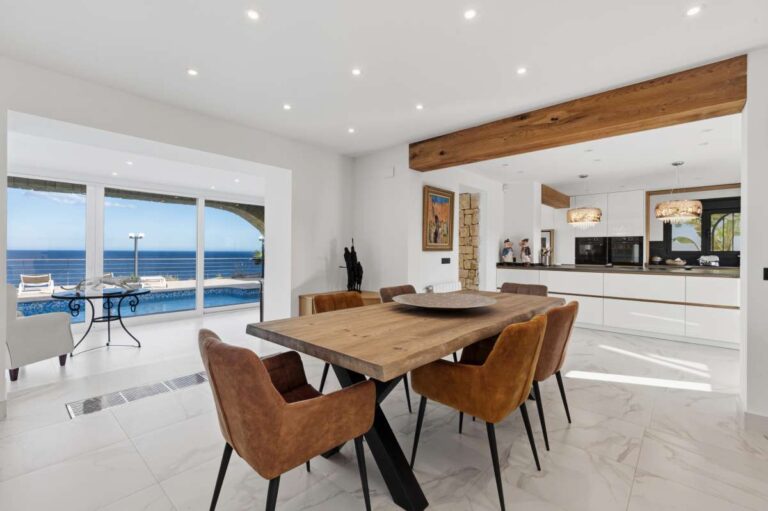 Dining area inside a premium coastal villa on the Benissa Costa with sea views, modern kitchen, wooden dining table and bright open-plan layout