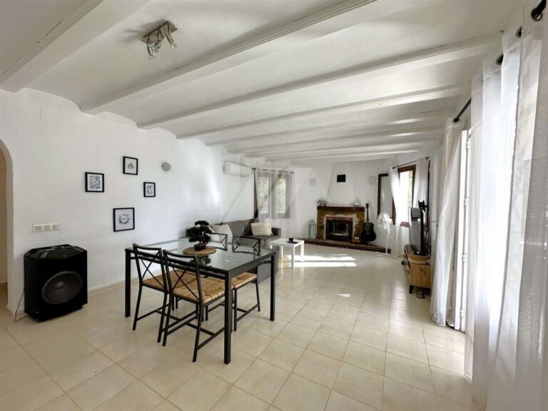 Dining area inside a single-level villa near El Portet Beach in Moraira with open living space, fireplace, white beamed ceiling and bright interior