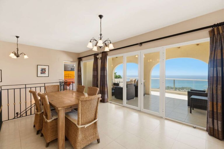 Dining area inside an Altea Hills villa with sliding doors to the panoramic terrace and Mediterranean Sea views beyond