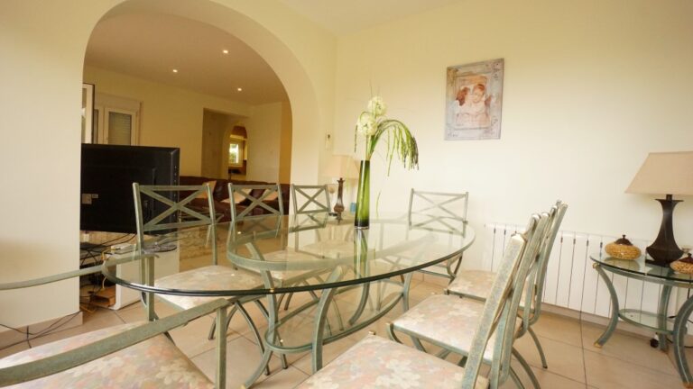 Dining area with glass table and arched opening inside a villa near La Fustera beach.
