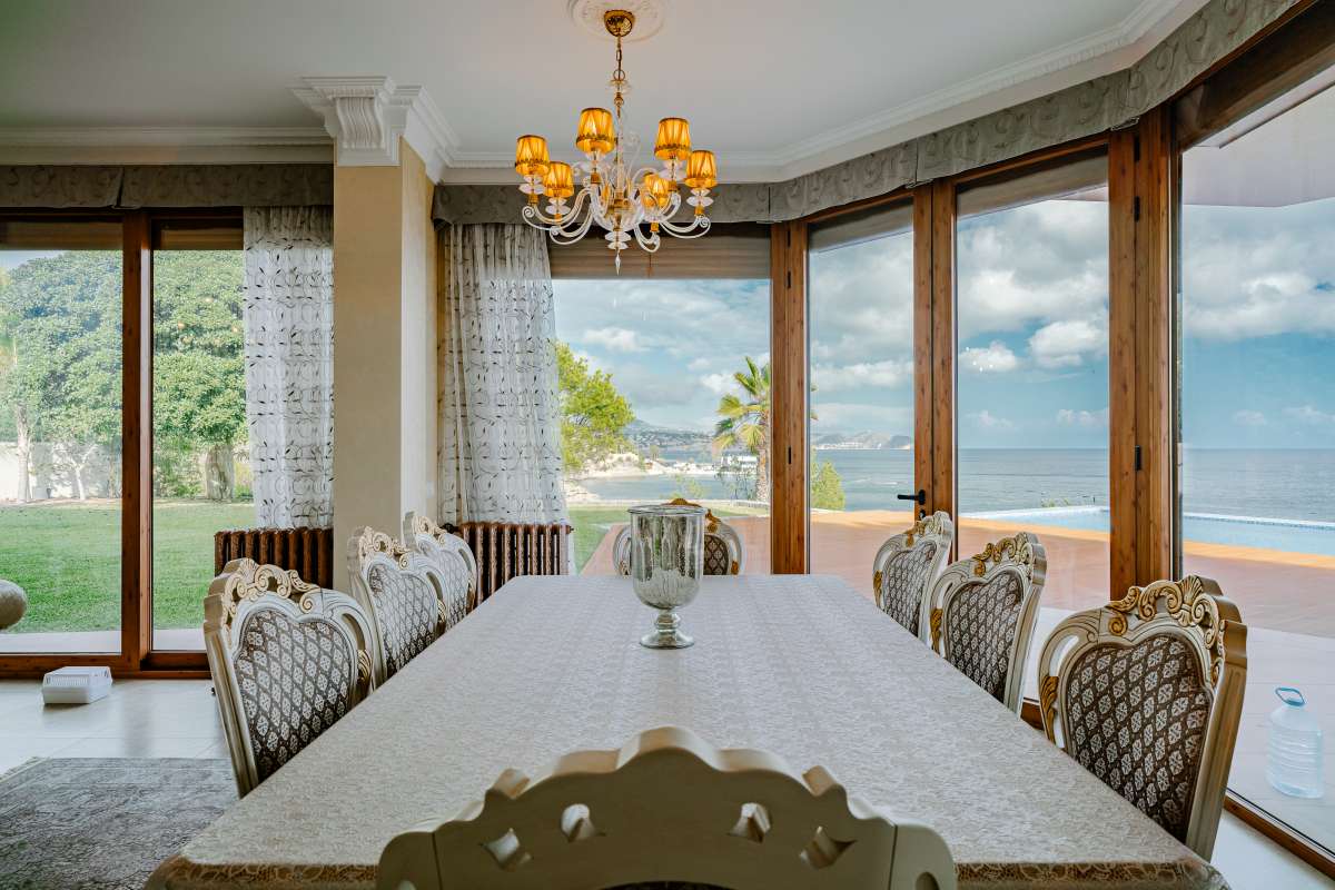 Dining area with large windows and coastal views inside a frontline villa in Les Bassetes, Benissa Coast.