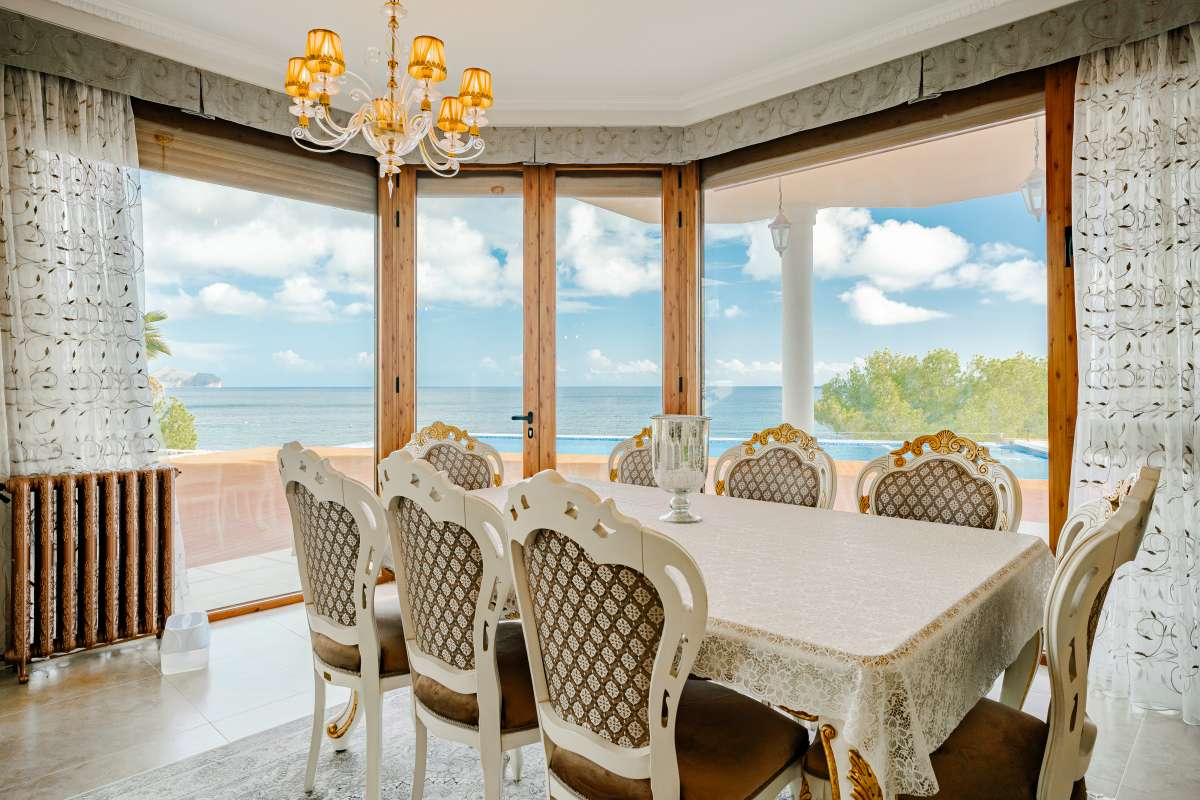 Dining area with large windows and sea views inside a frontline villa in Les Bassetes, Benissa Coast.