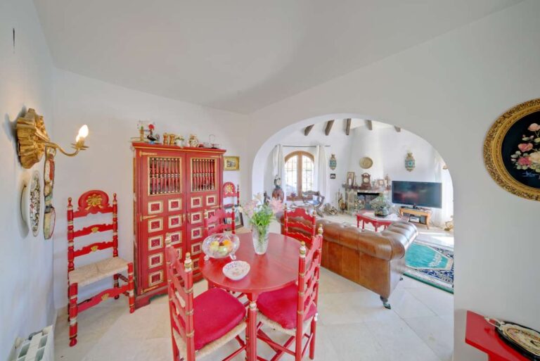 Dining area with traditional red furniture and arched opening inside a second line Mediterranean villa near Puerto Blanco in Calpe.
