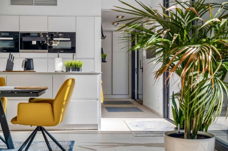 Dining area with yellow chair, kitchen view and tropical planting inside a modern oasis villa in Calpe.