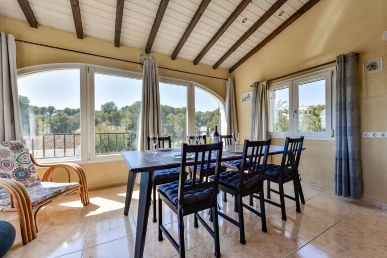 Dining room inside a charming Benissa Coast villa with beamed ceiling, arched windows, dining table and garden views