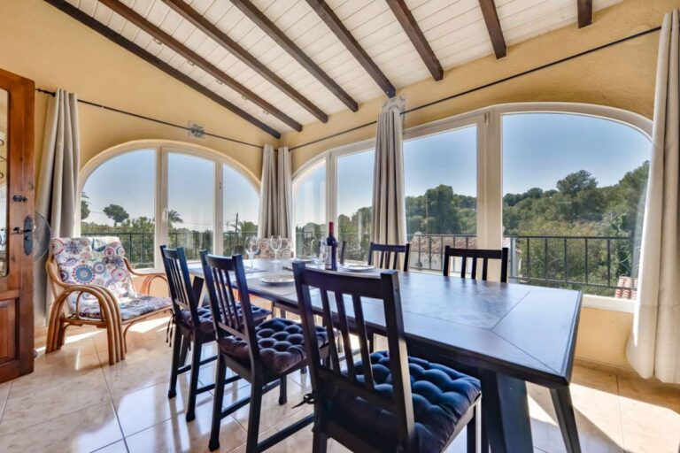 Dining room inside a charming Benissa Coast villa with beamed ceiling, arched windows, dining table and views across the terrace and garden