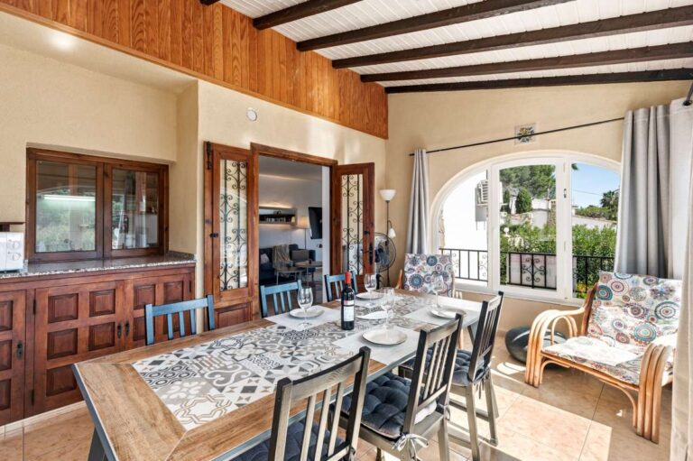 Dining room inside a charming Benissa Coast villa with beamed ceiling, dining table, serving area, arched windows and terrace access