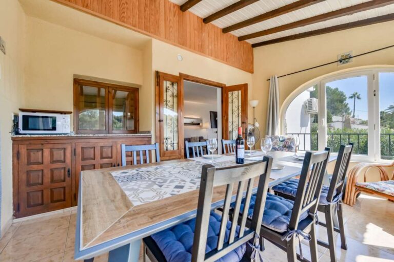 Dining room inside a charming Benissa Coast villa with beamed ceiling, serving area, large windows and access to the living area