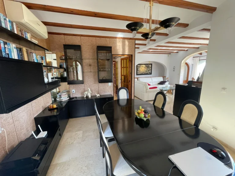 Dining room with wood-beamed ceiling and adjoining living area inside a villa in Calpe.
