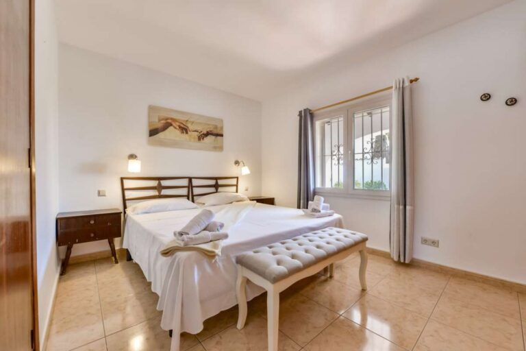 Double bedroom inside a charming Benissa Coast villa with bedside lighting, window, tiled floor and bright neutral interior