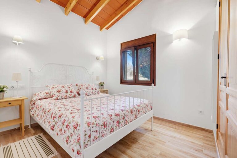 Double bedroom inside the guest house of a traditional Spanish finca near Moraira with wooden ceiling, window, bedside lighting and bright rustic finish