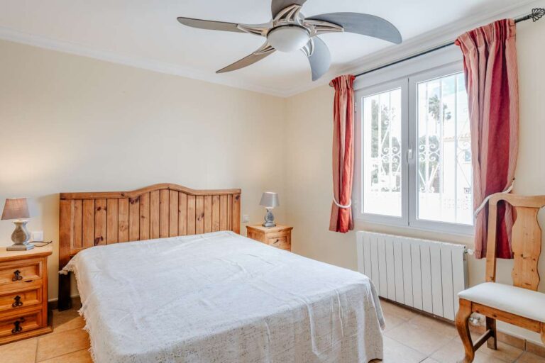Double bedroom with traditional wooden furniture, ceiling fan and natural light inside a Mediterranean villa in Calpe.