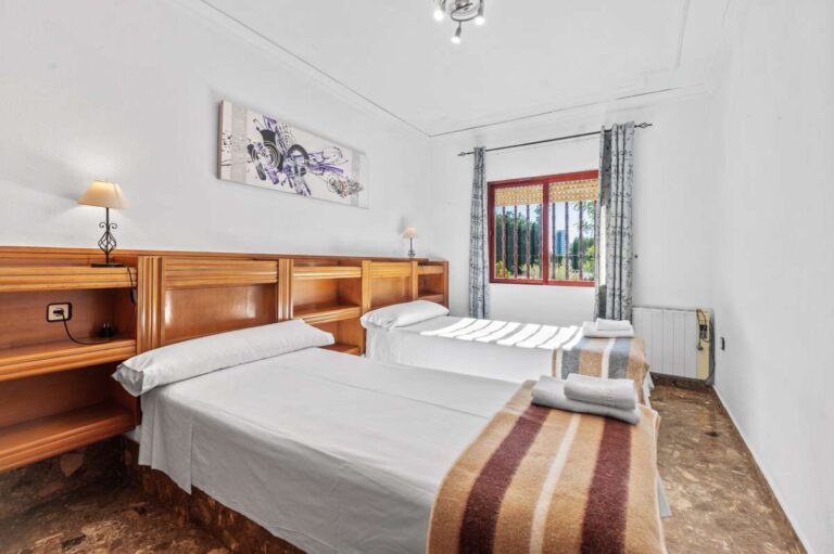 Double bedroom with wooden furniture and natural light inside a spacious villa with guest apartments in Calpe.