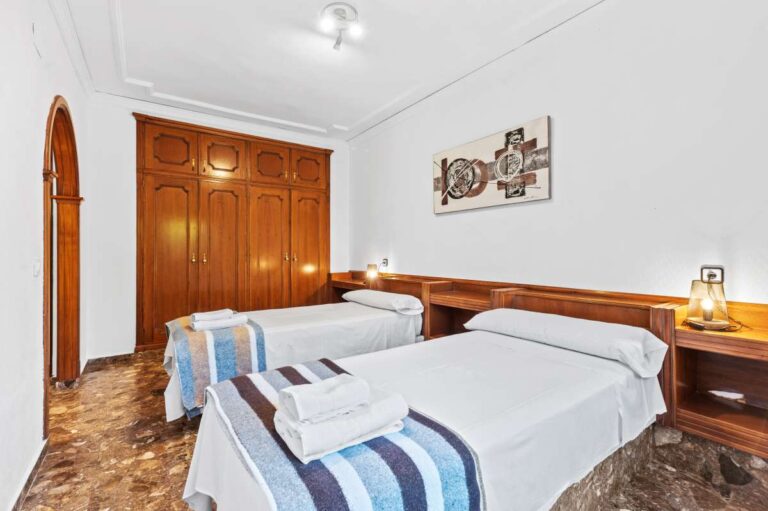 Double bedroom with wooden furniture, bedside lighting and tiled flooring inside a spacious villa with guest apartments in Calpe.