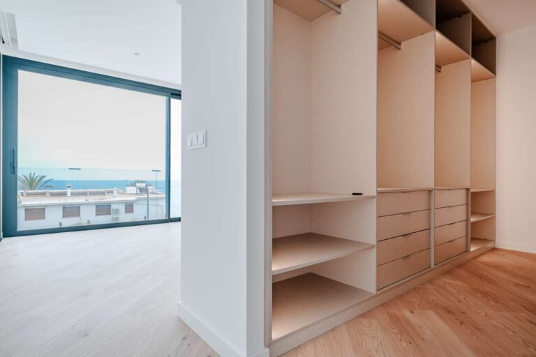 Dressing room inside a modern villa in La Calalga, Calpe with fitted wardrobes, wood finish and sea views from the bedroom area