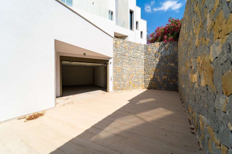 Zufahrt und Garagenzugang zu einer neu gebauten Luxusvilla in der Nähe des Yachthafens Puerto Blanco in Calpe mit Steinmauern, moderner Architektur und gepflastertem Eingangsbereich