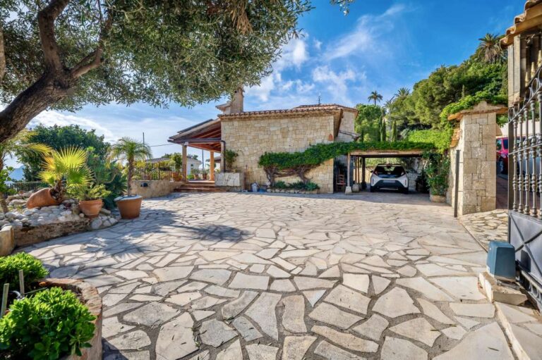 Driveway at a finca-style villa in Benissa Costa with stone paving, covered parking, Mediterranean planting and rustic villa exterior