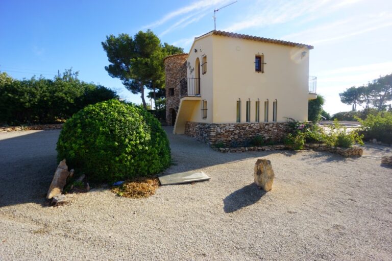 Driveway at a Mediterranean villa in Calpe with gravel parking area, mature garden planting and traditional villa exterior