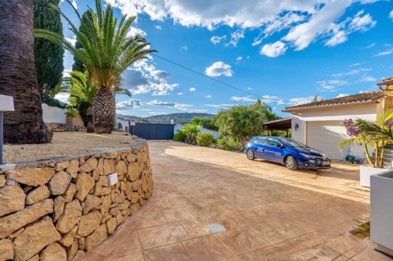 Driveway at a premium coastal villa on the Benissa Costa with private parking, stone walling, palm tree and sea views in the distance