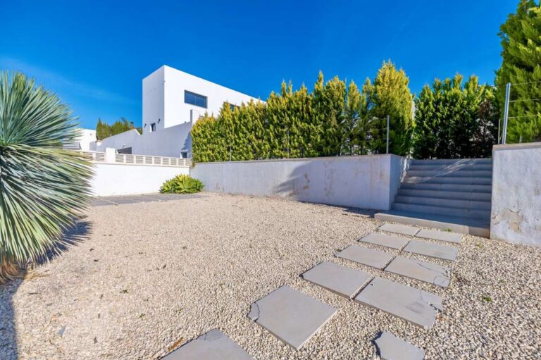 Driveway entrance with gravel parking, stepping stone path and landscaped garden at a modern oasis villa in Calpe.