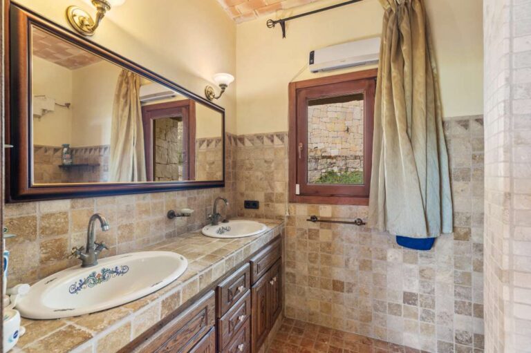En-suite bathroom inside a finca-style villa in Benissa Costa with double vanity, tiled walls, mirror and rustic Mediterranean finish