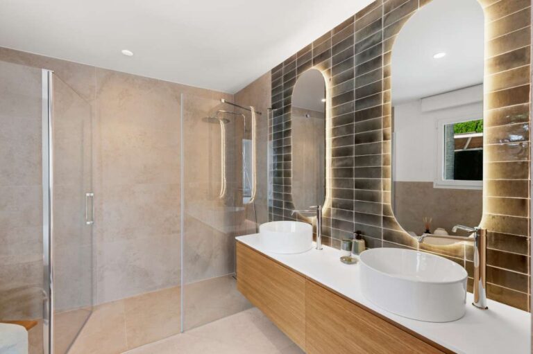 En-suite bathroom inside a modern villa in Altea Hills with walk-in shower, double vanity, illuminated arched mirrors and warm tiled finish