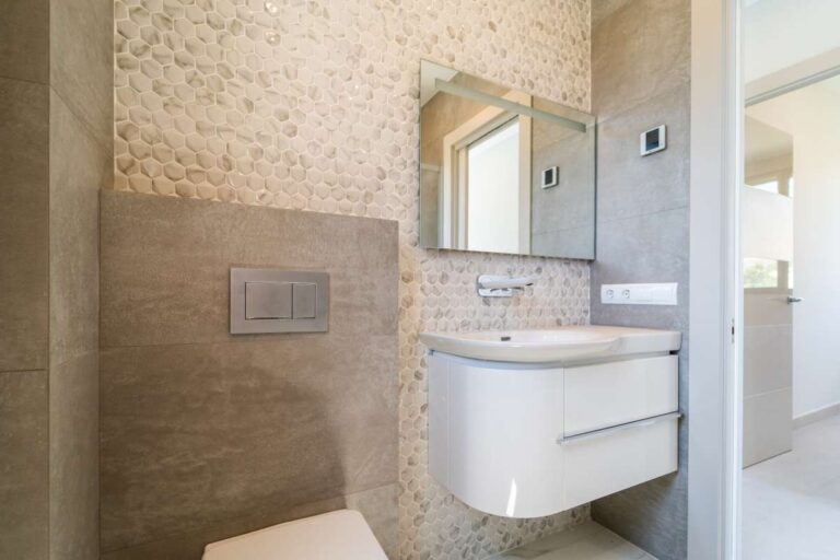 Das Badezimmer en suite in einer neu erbauten Luxusvilla in der Nähe des Yachthafens Puerto Blanco in Calpe verfügt über einen Waschtisch, ein wandhängendes WC, einen Spiegel und moderne Fliesen.