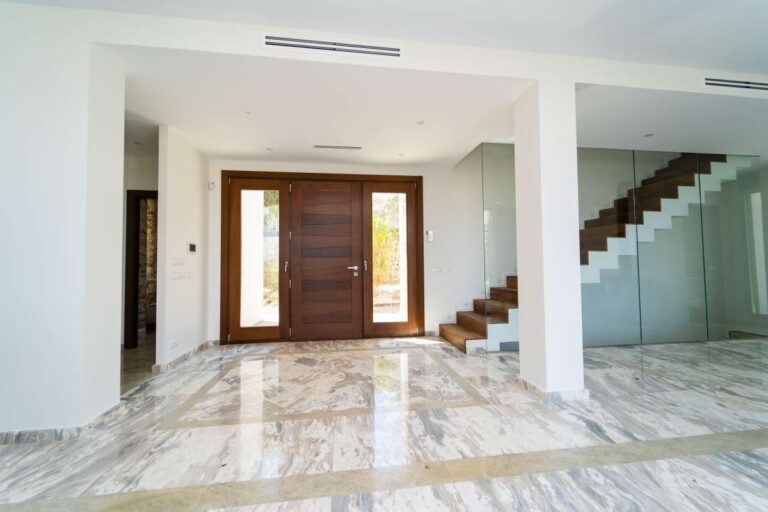 Entrance hall inside a luxury villa in Calpe with marble flooring, large wooden doors, glass staircase and spacious interior layout