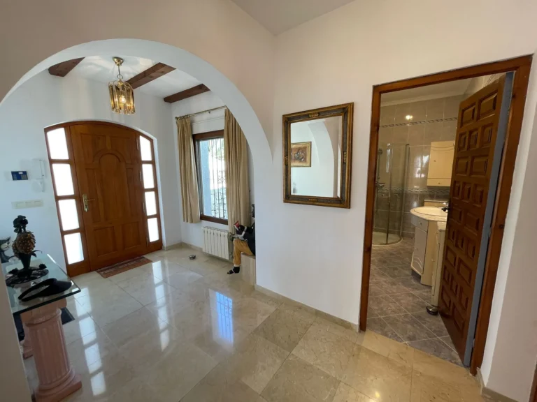 Entrance hall with wooden front door, bathroom access, tiled floor, and radiator inside a villa in Calpe.