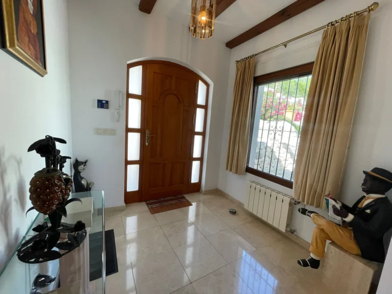 Entrance hall with wooden front door, tiled floor, and radiator inside a villa in Calpe.