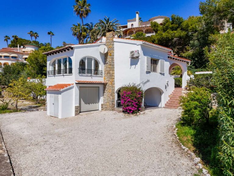 Exterior of a charming Benissa Coast villa with gravel driveway, garage, arched windows, red-tiled roof and Mediterranean garden surroundings