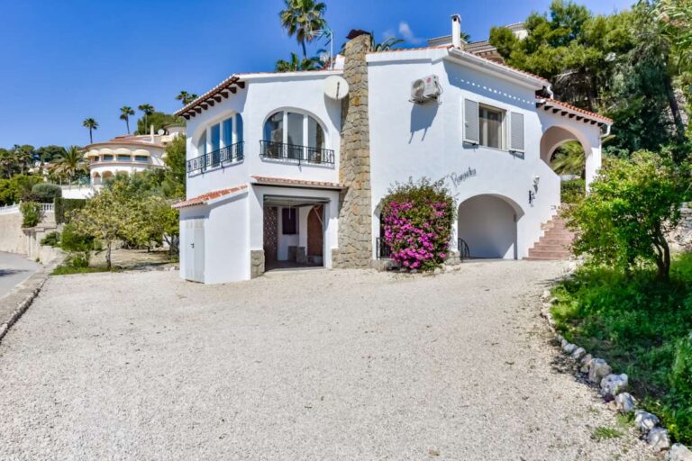 Exterior of a charming Benissa Coast villa with private driveway, garage, arched windows, red-tiled roof and Mediterranean garden surroundings