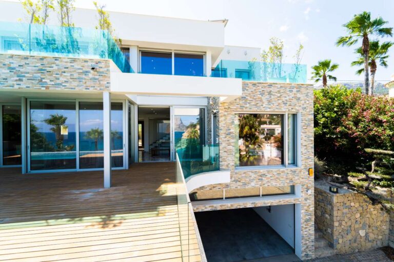 Exterior of a luxury villa in Calpe with stone façade, large terrace, garage access, glass balustrades and poolside outdoor space