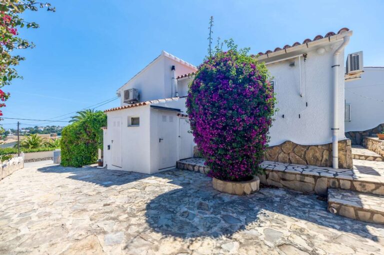 Exterior of a renovated single-level villa in Moraira with stone paving, flowering bougainvillea, white façade and Mediterranean garden details