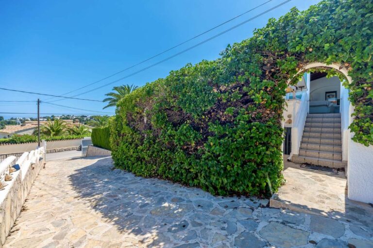 Exterior steps at a renovated single-level villa in Moraira with stone paving, white walls, flowering greenery and Mediterranean garden access