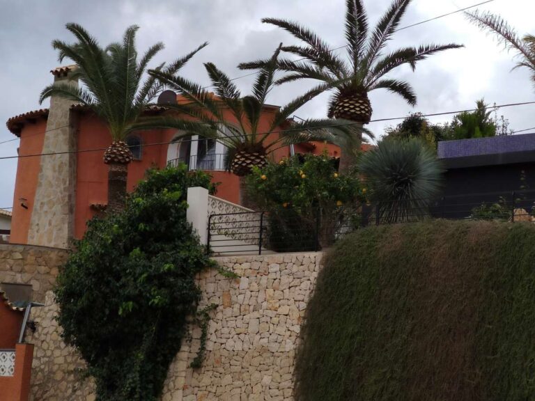 Exterior view of a Mediterranean villa with palm trees and stone wall in the quiet residential area of Canuta, Calpe.