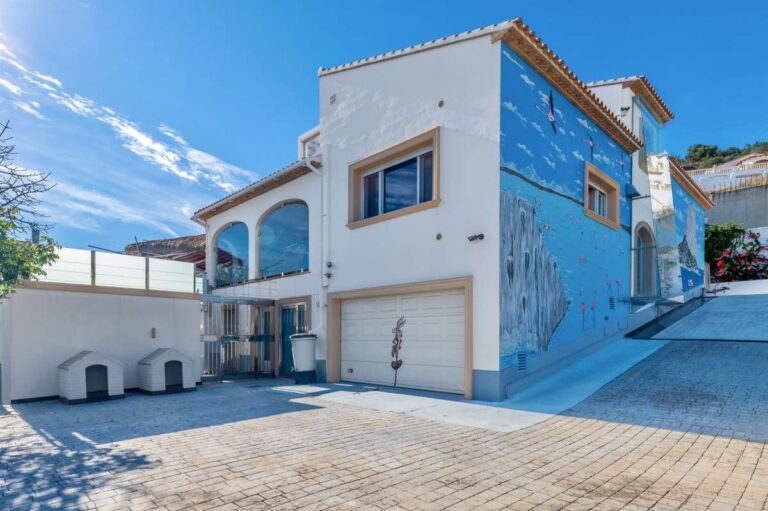 Exterior view of a private villa in Calpe with closed garage, arched terrace, driveway and open sea views in the distance
