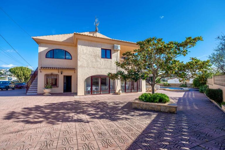 Exterior view of a spacious villa in Calpe with driveway, arched windows and parking area.