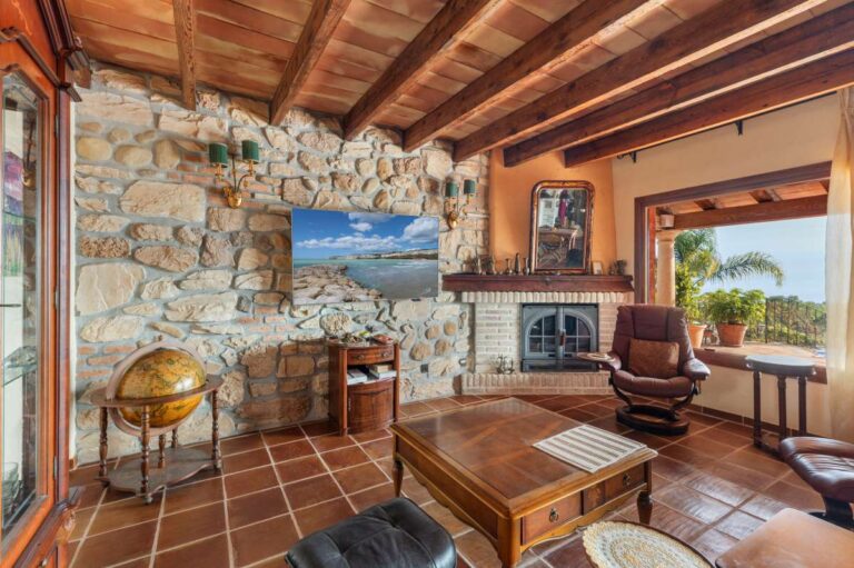 Fireplace lounge inside a finca-style villa in Benissa Costa with natural stone wall, wooden beams, terracotta tiled floor and rustic seating