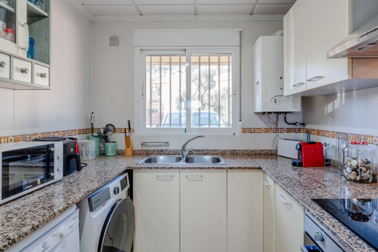Fitted kitchen inside a semi-detached house in Calpe with appliances, washing machine, tiled walls and natural light