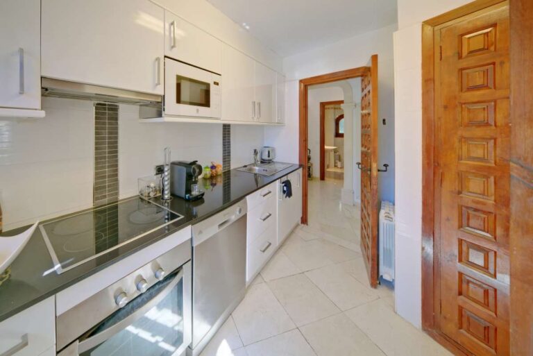 Fitted kitchen with white cabinets and wooden door inside a second line Mediterranean villa near Puerto Blanco in Calpe.
