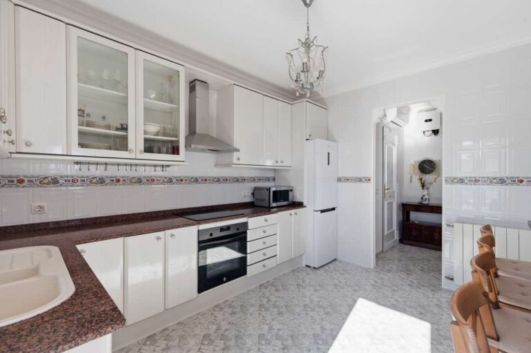Fitted kitchen with white cabinets, oven, and natural light inside a villa in Calpe.