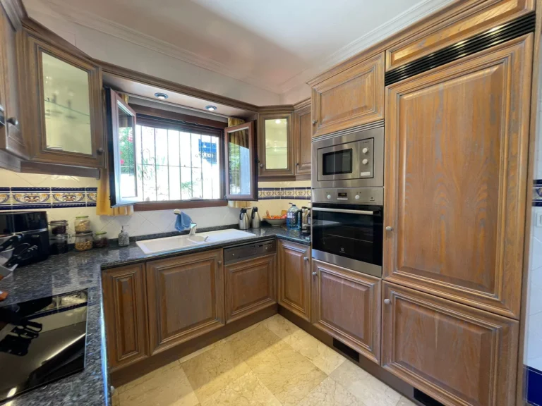 Fitted kitchen with wood cabinets, integrated appliances, and granite worktops inside a villa in Calpe.