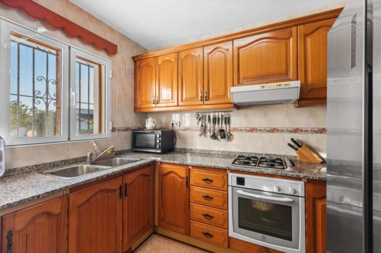 Fitted kitchen with wooden cabinets and natural light inside a single-level villa in Calpe close to beaches and amenities.