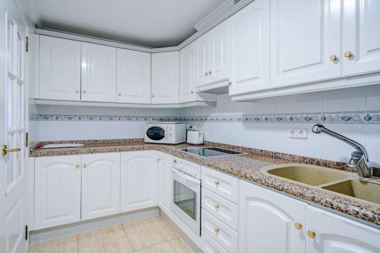 Fully equipped kitchen inside a duplex apartment near Les Platgetes Beach in Moraira with white cabinetry, granite worktops and built-in appliances