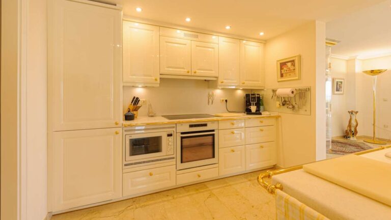 Fully equipped kitchen inside a luxury apartment in Sierra de Altea with white cabinetry, marble flooring, integrated appliances and bright lighting